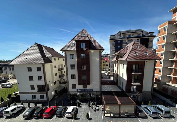 A multi-story residential building with a central courtyard, parking area, and a sign reading "ALL SEASONS".