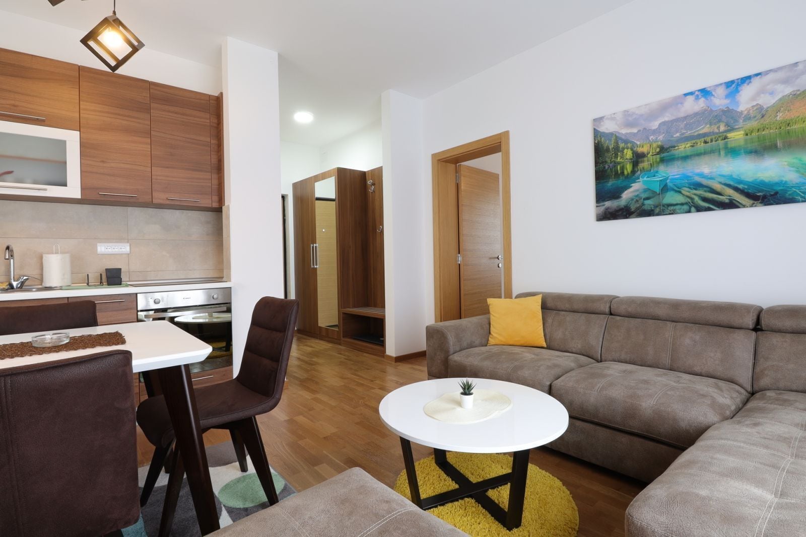 A modern living room with a grey sofa, a small white table, and a dining area with a table and chairs.