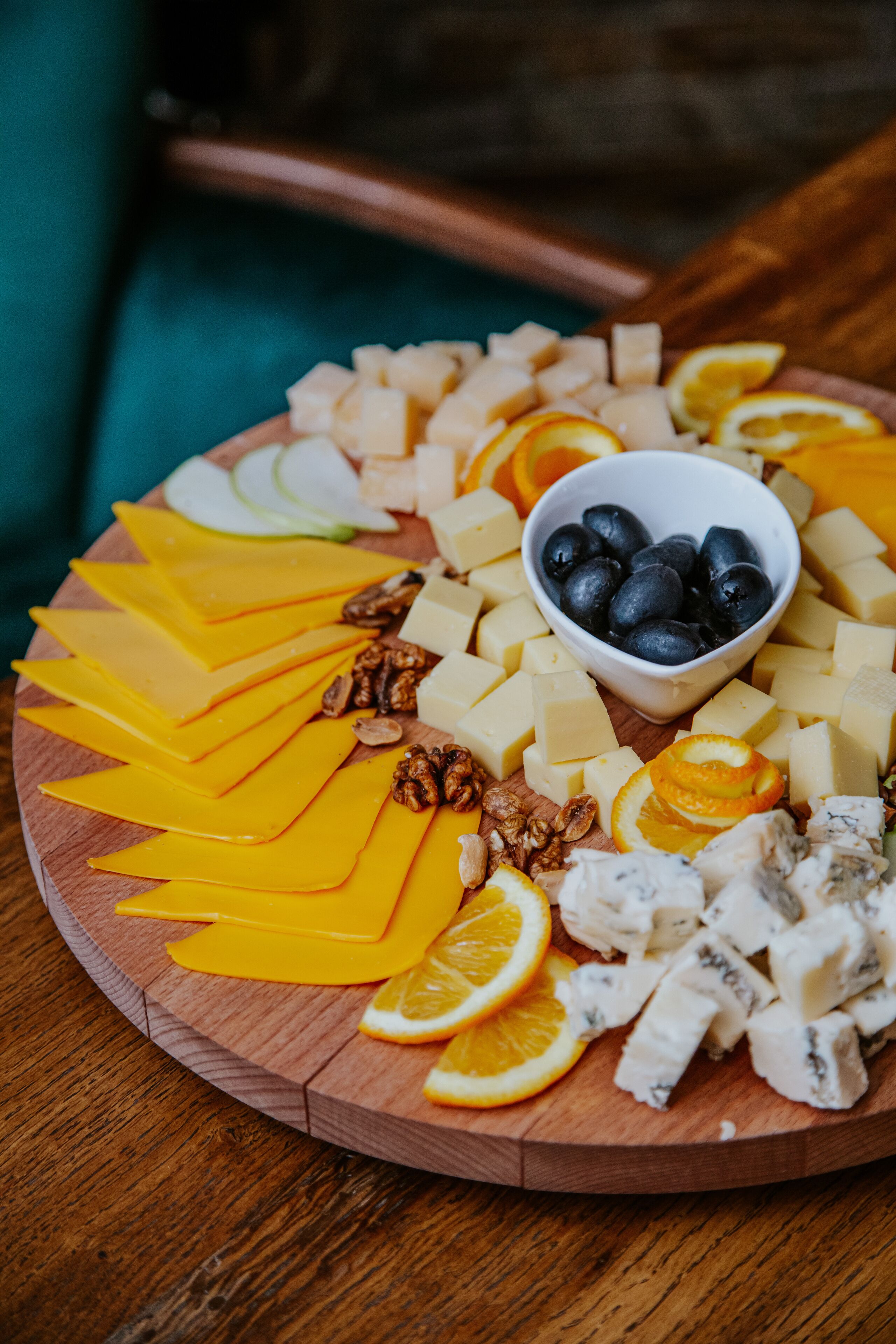 A wooden board with various cheeses, fruits, and nuts arranged on a table.