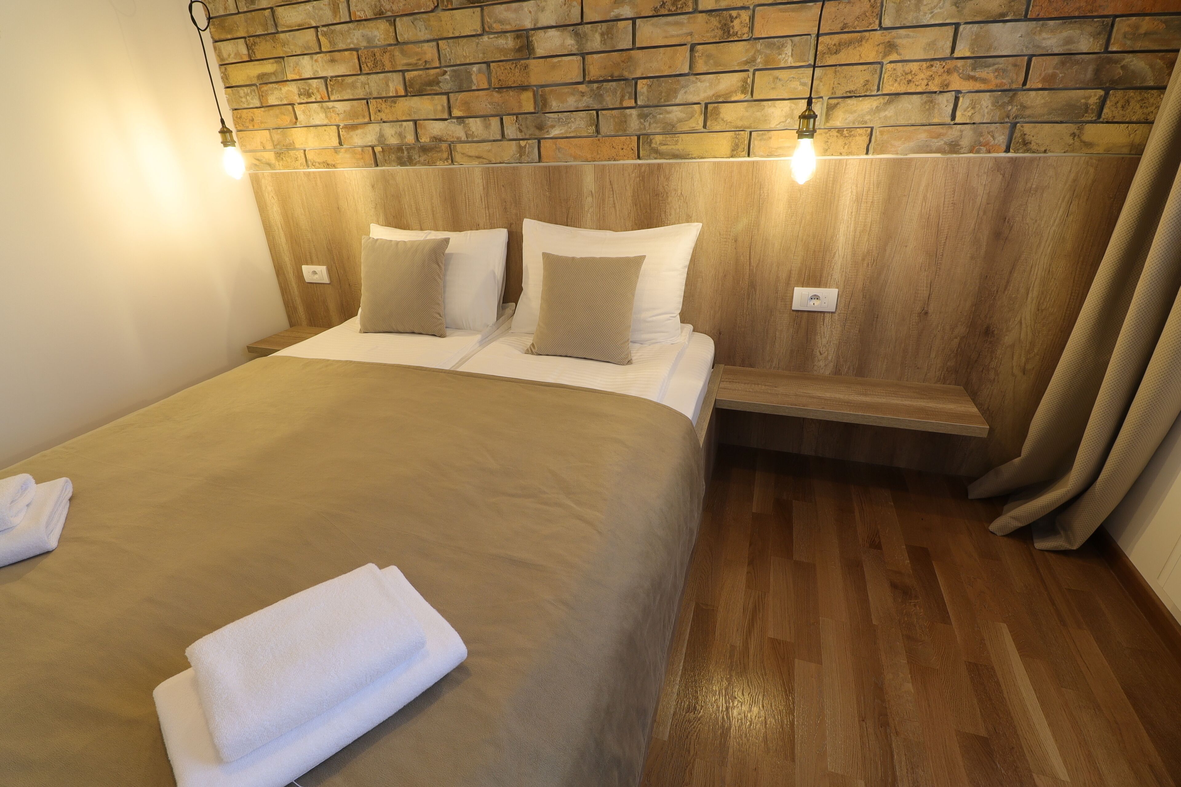 Ein ordentlich bezogenes Bett mit Holz-Kopfteil, zwei Kissen und einer Bank am Fußende.