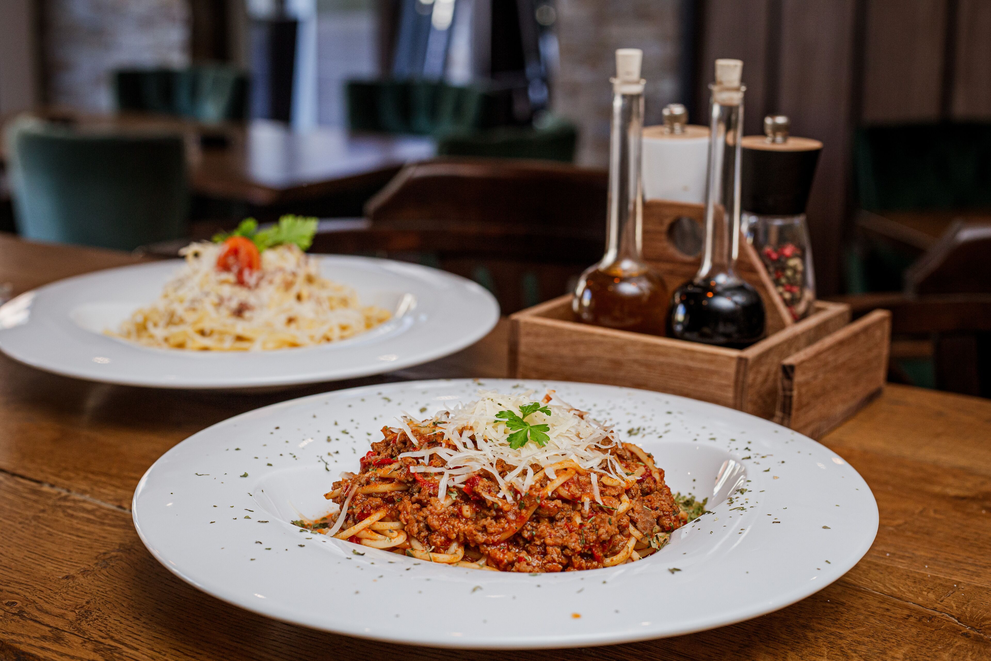Two plates of spaghetti on a wooden table with salt and pepper shakers in the background.