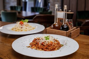Two plates of spaghetti on a wooden table with salt and pepper shakers in the background.