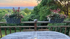 A round wooden table with two chairs, surrounded by a wooden railing, with hanging planters on either side. - Mountain-view House ~ Mins To Middlebury, Flex Cancellation Policy (Cornwall)