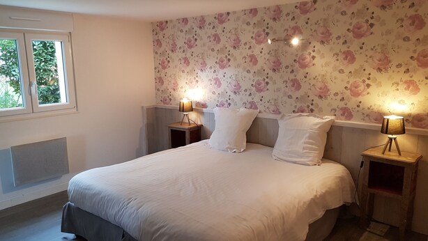 Een slaapkamer met een groot bed, bloemenbehang, twee bedlampen en een raam met zonwering.
