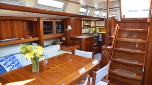 Interior de un barco con comedor, cocina y una escalera.