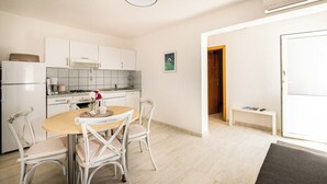 Cozinha compacta com armários brancos, uma mesa de jantar com quatro cadeiras e um pequeno banco perto da porta.