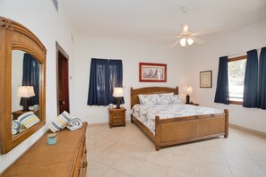 Un dormitorio con una cama de madera, dos mesitas de noche con lámparas, un espejo grande y un ventilador de techo.