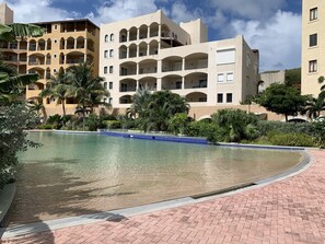 Un resort con una piscina grande, palmeras y edificios de varios pisos con balcones.
