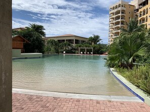 Una piscina con borde de azulejos, rodeada de vegetación y un edificio con varios balcones.