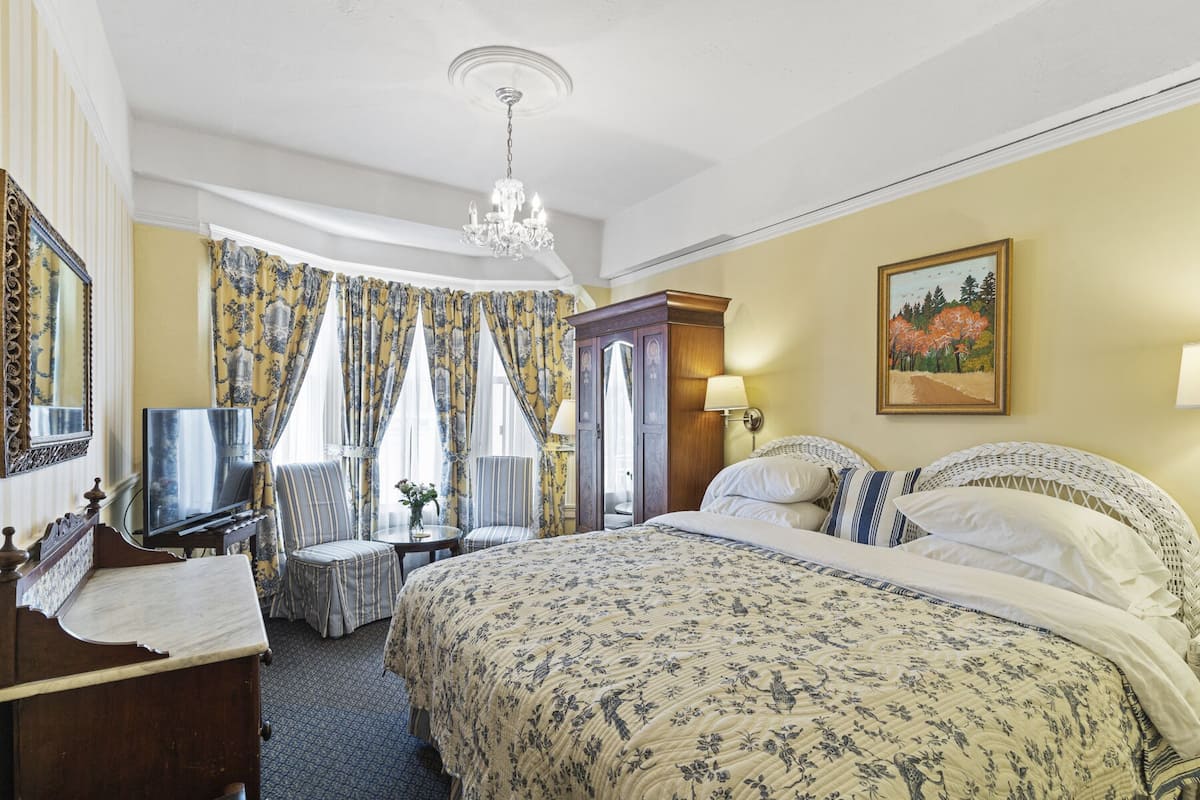 A hotel room with a large bed, a television, a desk, and a chair.