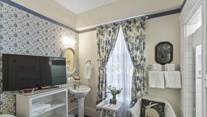 A bathroom with a television, sink, mirror, and a wicker chair.