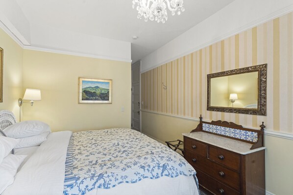 A hotel room with a bed, a dresser, a mirror, a lamp, and a painting on the wall. - Golden Gate Hotel (San Francisco)