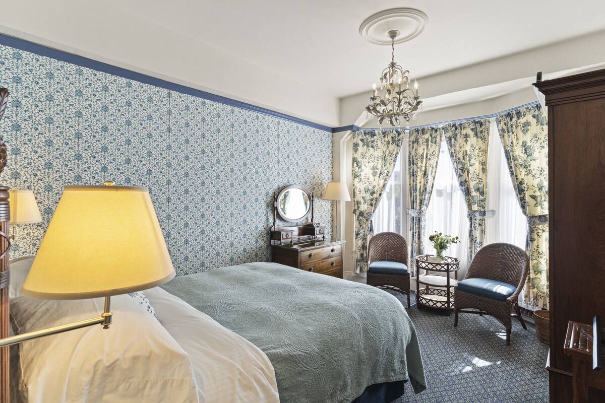 A bedroom with a bed, two chairs, a dresser, a mirror, and a chandelier.