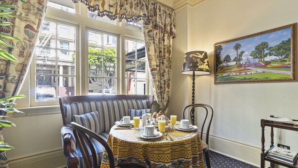 A dining area with a table set for breakfast, a bench, and a painting on the wall.