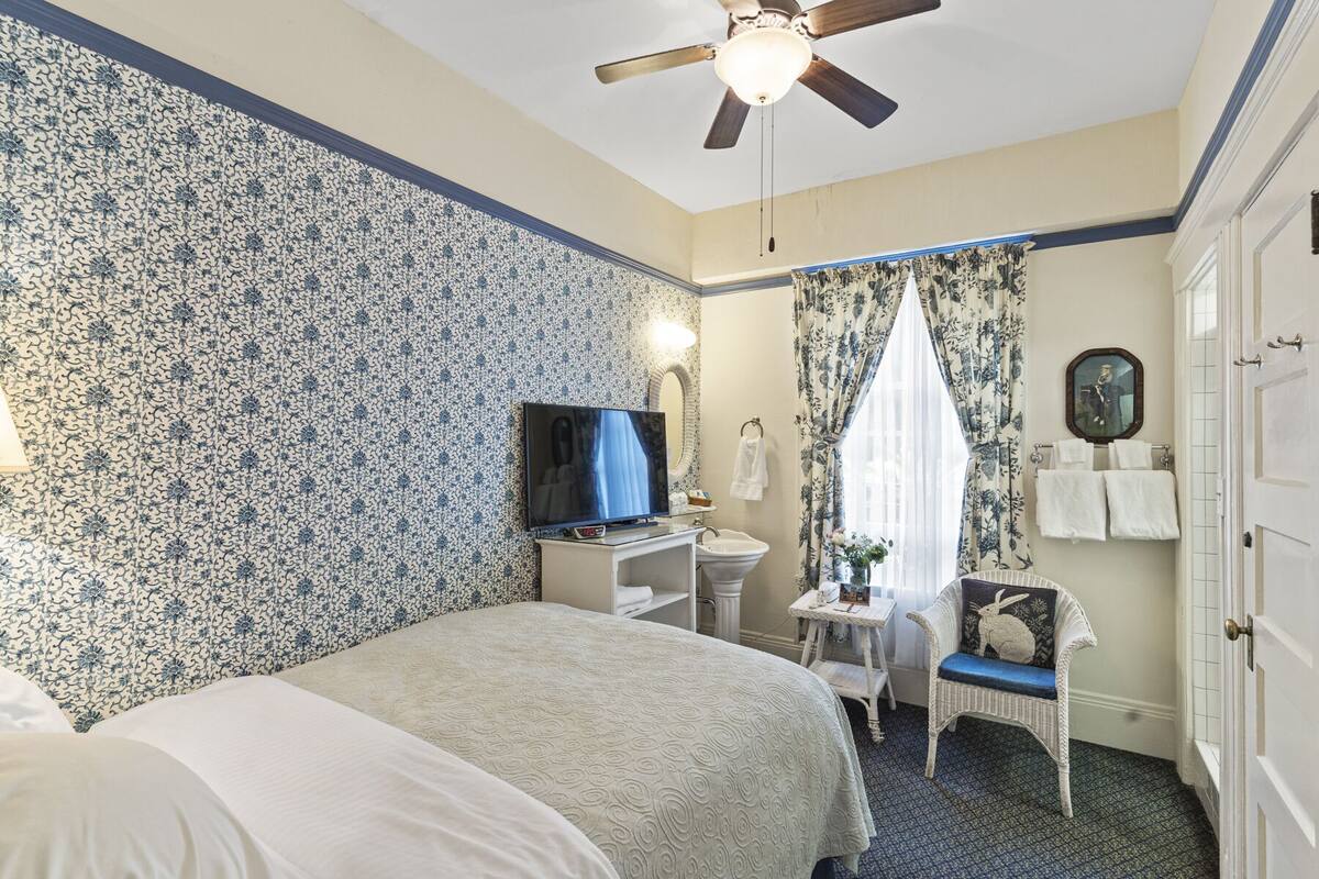 A hotel room with a bed, a desk, a television, a chair, a wardrobe, and a ceiling fan.
