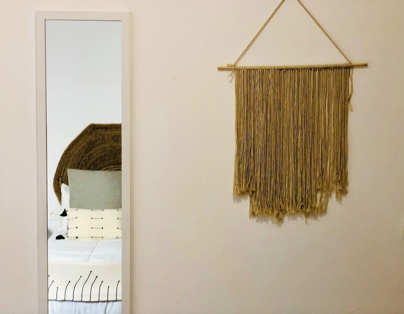 Una stanza con un letto, un arazzo macramè appeso al muro e uno specchio che riflette parte della stanza.