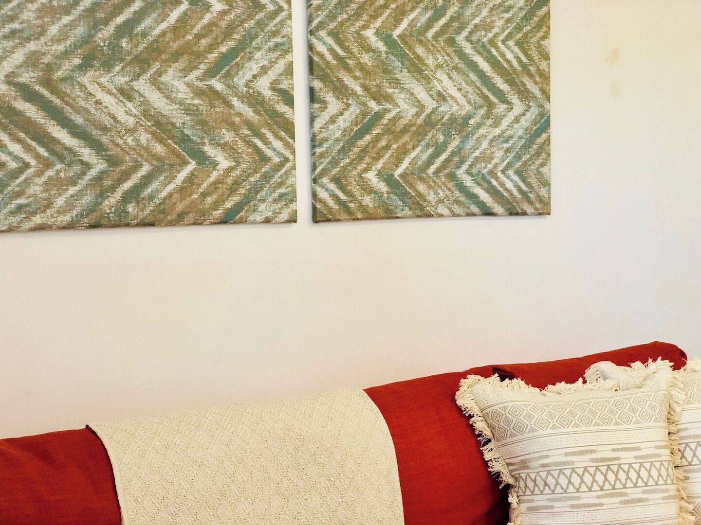A room with a sofa featuring a red and white cushion, a patterned throw blanket, and a chevron-patterned wall hanging.