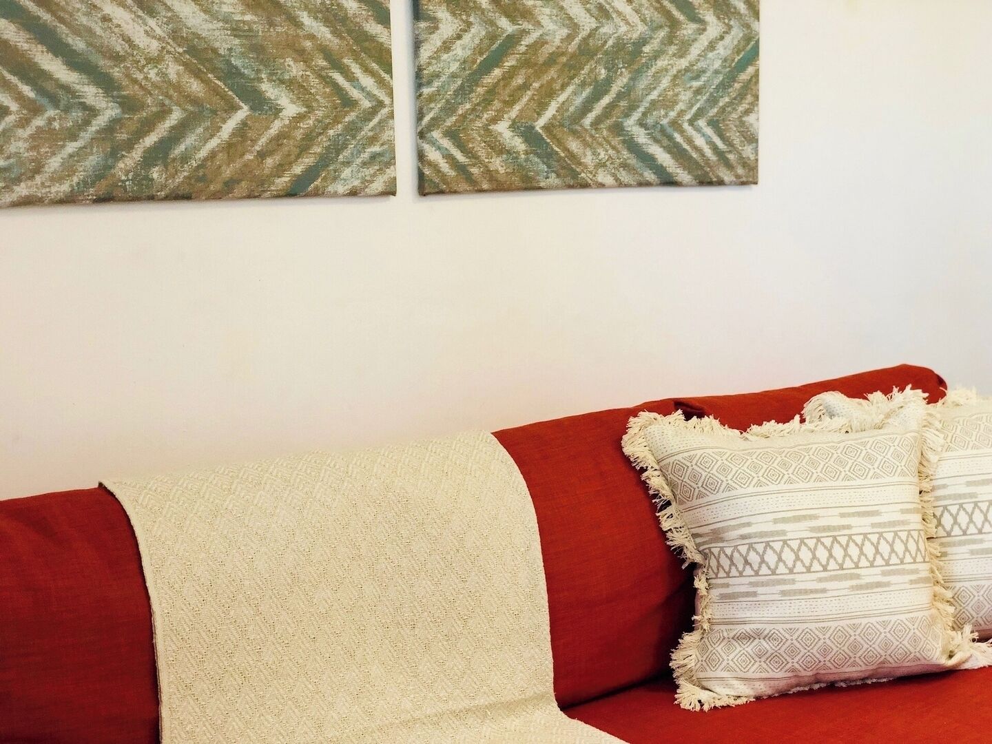 Un sofá rojo con una manta color beige y cojines estampados.