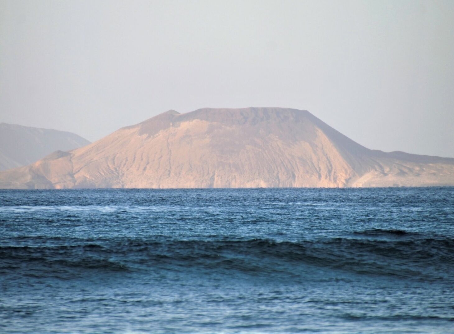A mountain range with a clear view of the sea in the foreground.