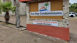 A sign for Sun Ray Condominiums with a logo featuring a house, palm tree, and sun. - Sun Ray #2B - Pet Friendly, 3min Walk to Beach (South Padre Island)