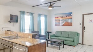 A compact living space with a kitchenette, a green sofa, a flat-screen TV, and a painting of a beach scene. - Sun Ray #2B - Pet Friendly, 3min Walk to Beach (South Padre Island)