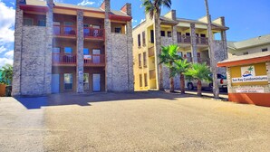 A multi-story building with balconies, palm trees, and a sign for Sun Ray Condominiums. - Sun Ray #2B - Pet Friendly, 3min Walk to Beach (South Padre Island)