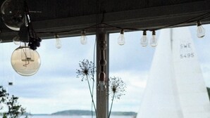 Una mesa de madera con tazones de comida, una cafetera y una vela. Se ve un velero a través de la ventana.