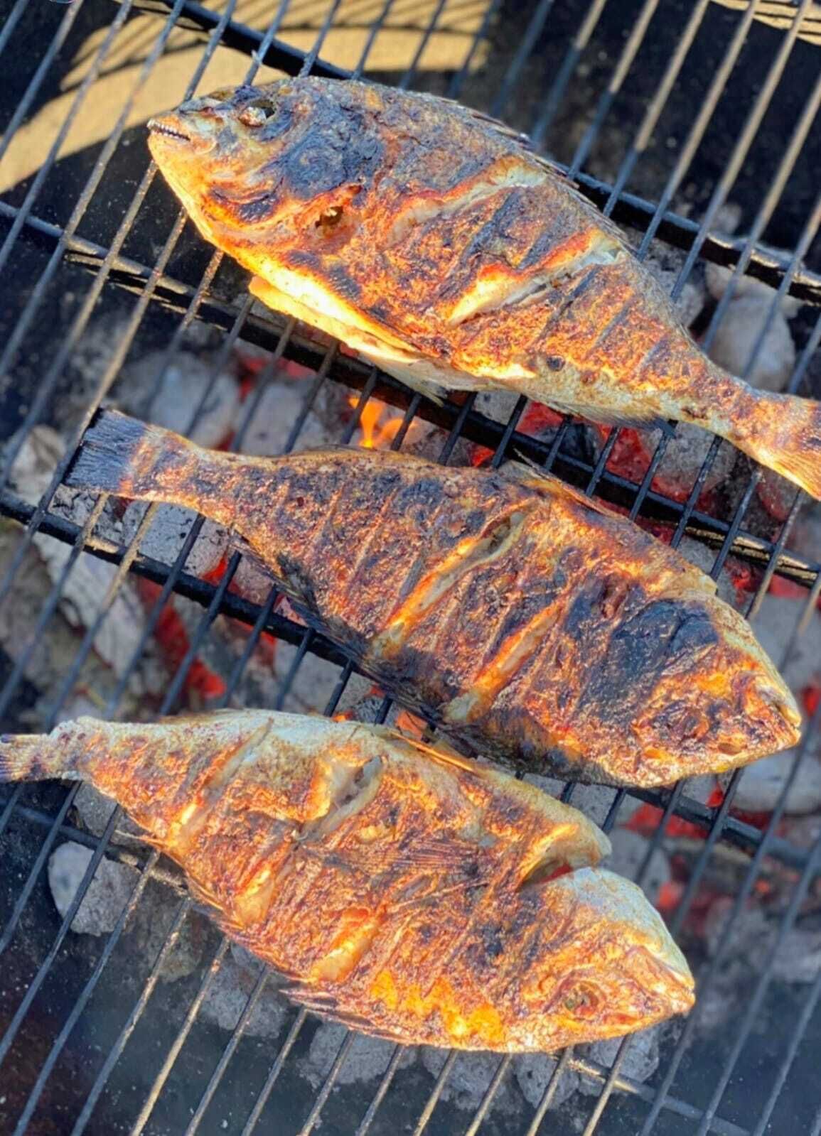 Three fish being grilled on a metal grate over an open flame.