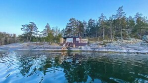 Una cabaña junto al lago con un balcón y escaleras que conducen a la entrada, rodeada de árboles y terreno rocoso.