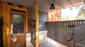 Eine rustikale Holzhütte mit Holztür, Grillrost und Betonboden.