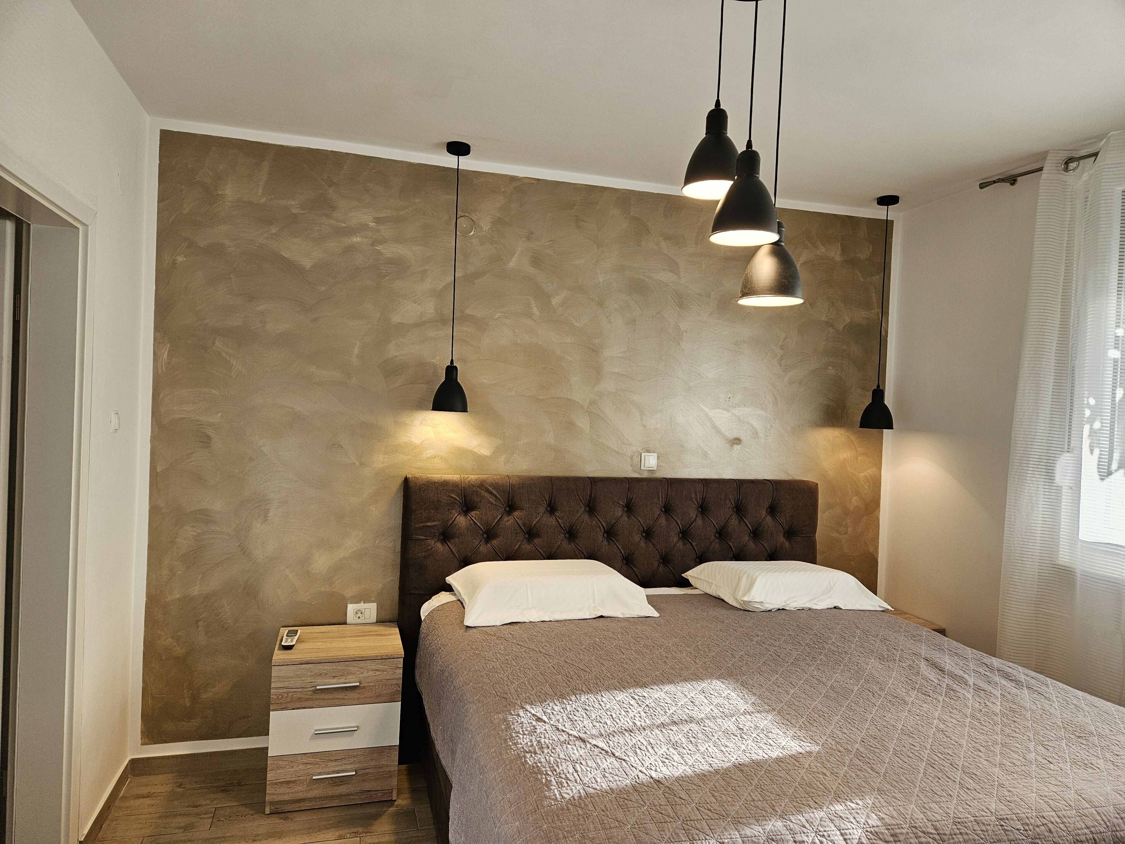 Een slaapkamer met een groot bed, twee bedlampjes, een nachtkastje en een structuurwand.
