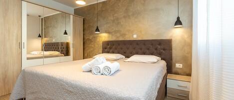 A bedroom with a large bed, a wardrobe, a mirror, and pendant lights.