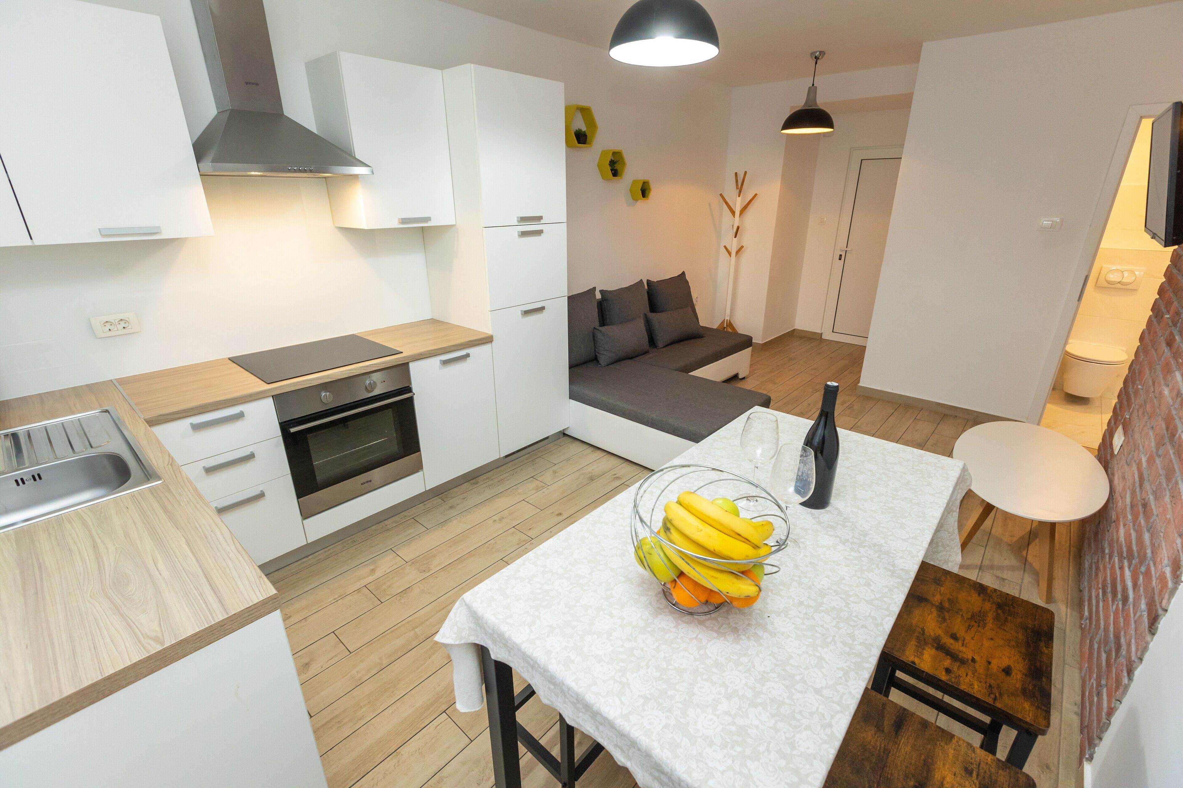 Une cuisine moderne avec des meubles blancs, un plan de travail en bois et un coin repas avec une table dressée pour deux personnes.