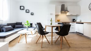A modern kitchen with white cabinets, a built-in oven, and a stainless steel range hood. There is a dining area with a round table and black chairs. - Deluxe Apartment near Bridge (Zadar)