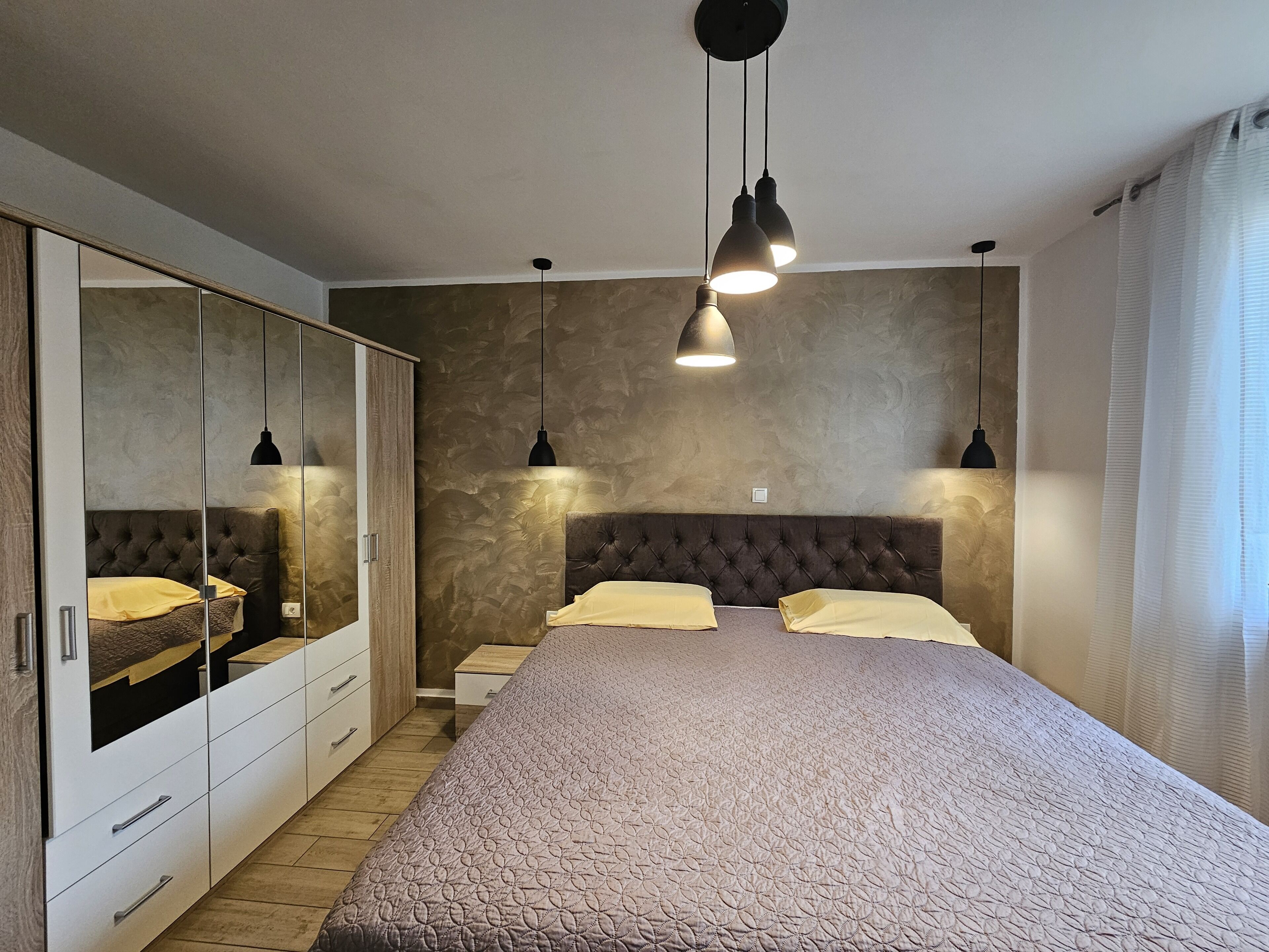 A bedroom with a large bed, a wardrobe, and pendant lights.