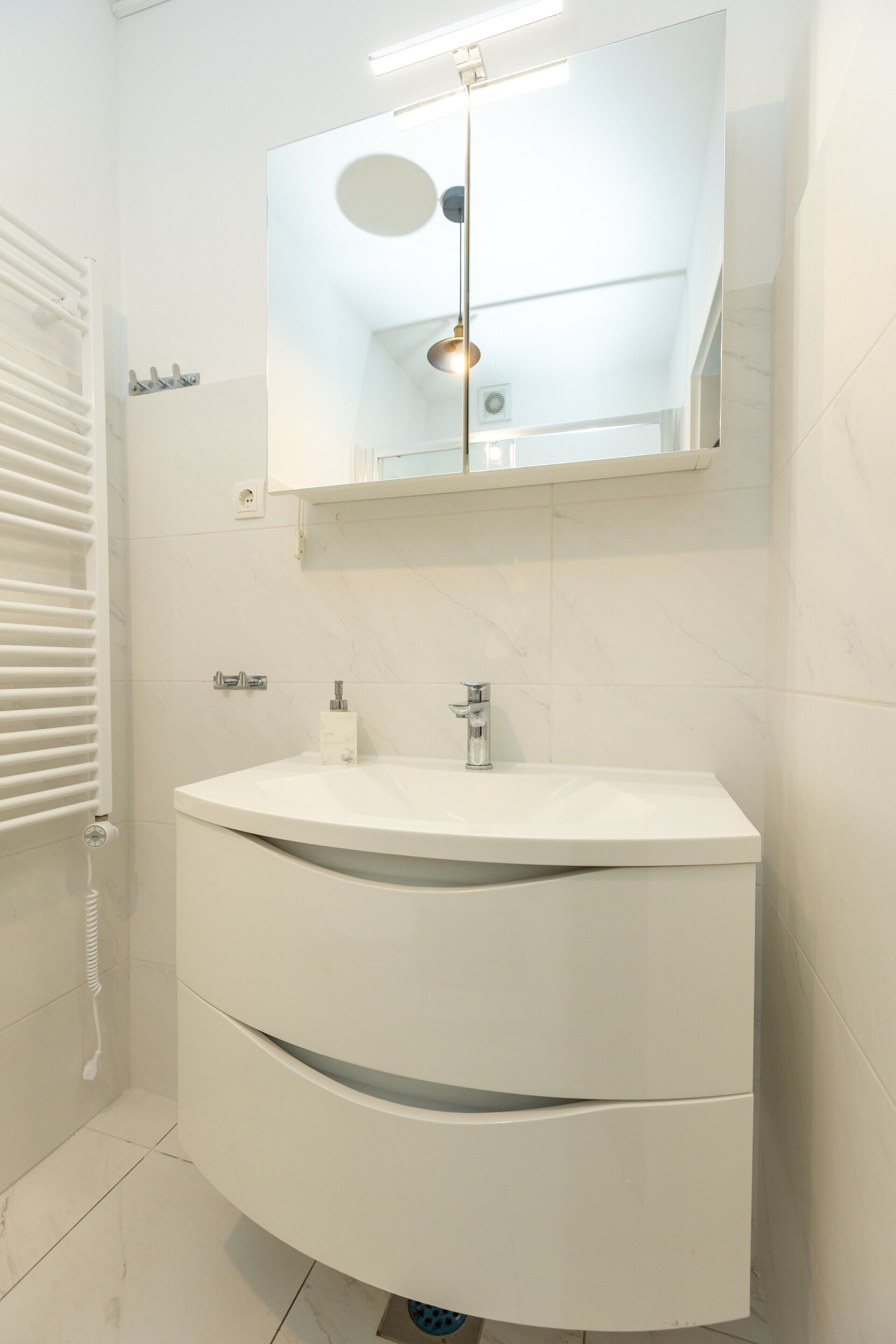 A modern bathroom with a white vanity, a mirror, and a towel rack.