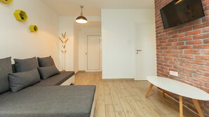 A modern living room with a grey sofa, a white table, a brick wall, and a mounted TV. - Deluxe Apartment near Bridge (Zadar)