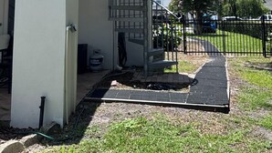 Un edificio residencial con una escalera de caracol, un camino de entrada con portón y un césped.