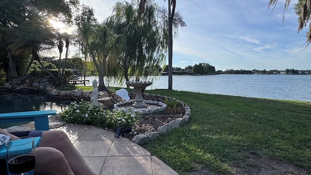 Un patio con una mesa de piedra, una copa de vino y vistas a un lago.