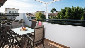 En balkon med et bord og stole, udsigt til bygninger og træer, og en klar himmel.