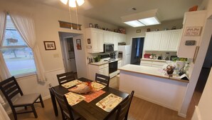 Una cocina moderna con armarios blancos, una isla central y un comedor con mesa y sillas de madera.