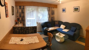Ein gemütliches Wohnzimmer mit einer Couch, einem kleinen Tisch und einem Fenster mit Vorhängen.