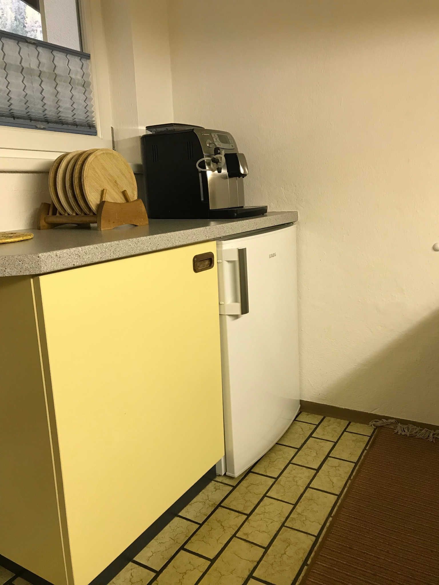 A compact kitchen with a coffee machine, a wooden cutting board, and a small refrigerator.