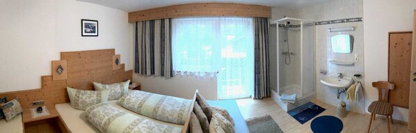 A bedroom with a bed, a wooden headboard, a shower, a sink, and a window with curtains.