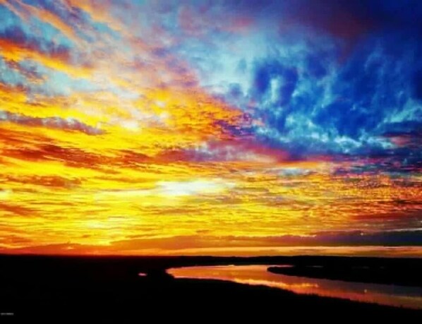 Een zonsondergang boven een wateroppervlak, met een donker silhouet van land voor op de voorgrond.