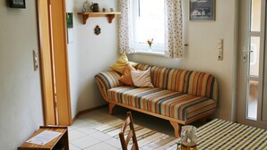 A cozy living room with a striped sofa, a dining table with a checkered tablecloth, and a window with curtains. - Cozy 3-star vacation home, quiet and close to nature for 4 people / 2 bedrooms (Zwiesel)