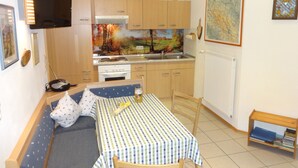 A compact kitchen with wooden cabinets, a built-in stove, and a sink. There's a dining area with a checkered tablecloth and a small bookshelf. - Cozy 3-star vacation home, quiet and close to nature for 4 people / 2 bedrooms (Zwiesel)