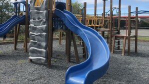 A playground with a blue slide, climbing structures, and a wooden playhouse.