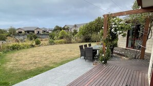 A wooden deck with a table and chairs, a garden area with grass and plants, and a cloudy sky.