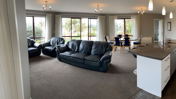 A modern living room with a leather sofa, dining area, and a kitchen with white cabinets and a granite countertop.